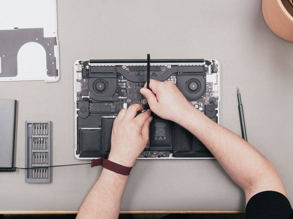 A technician's hands working inside an open laptop with a screwdriver